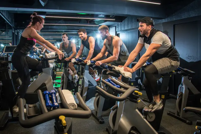 A fitness instructor on an exercise bike leads a class in a gym.